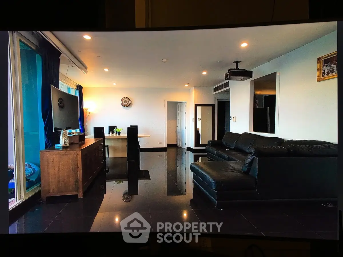 Spacious modern living room with sleek black leather sofa and large TV, perfect for entertainment.
