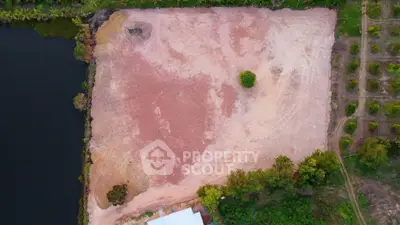 Aerial view of a large empty plot of land near a water body, ideal for development.