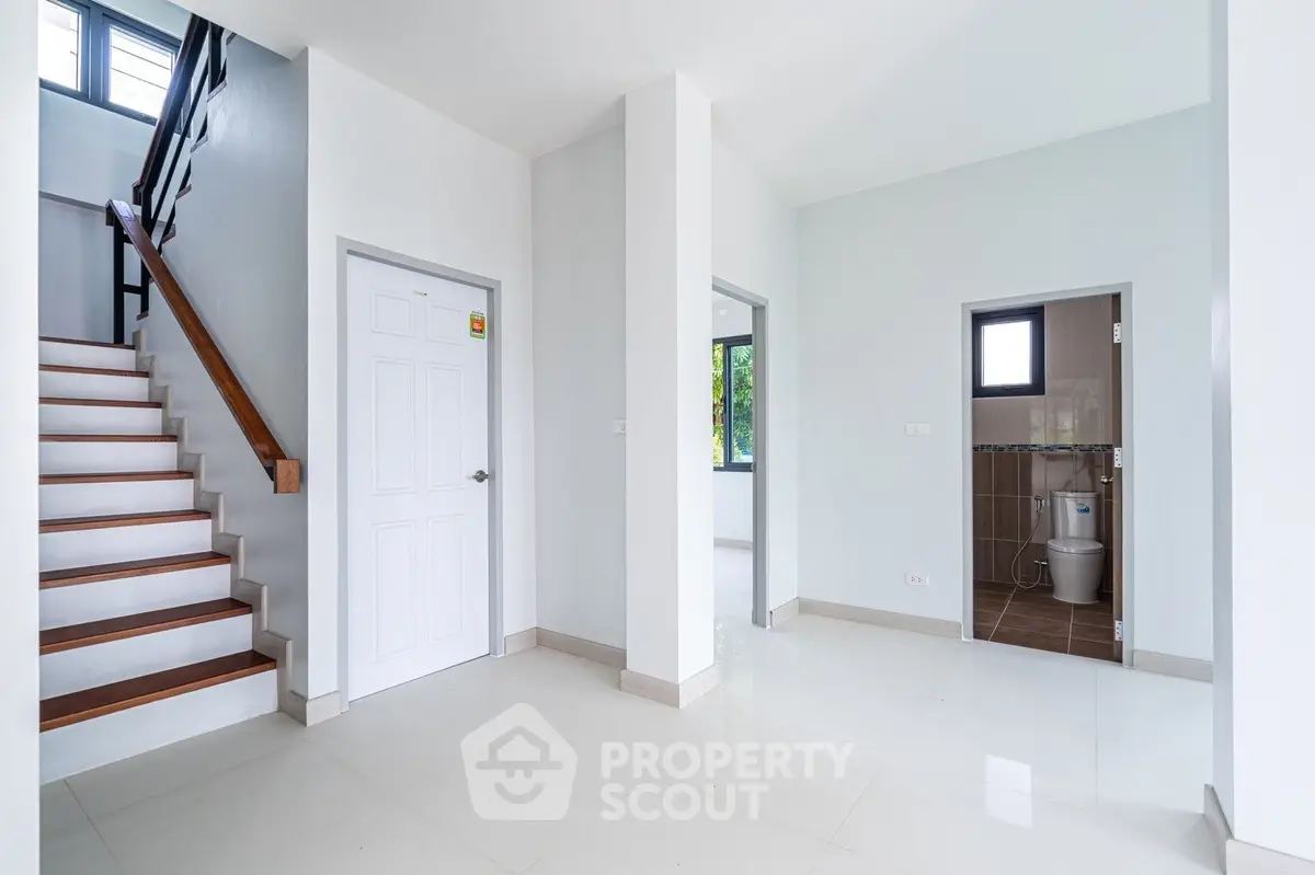 Spacious modern interior with staircase and bathroom, featuring sleek white tiles and natural light.