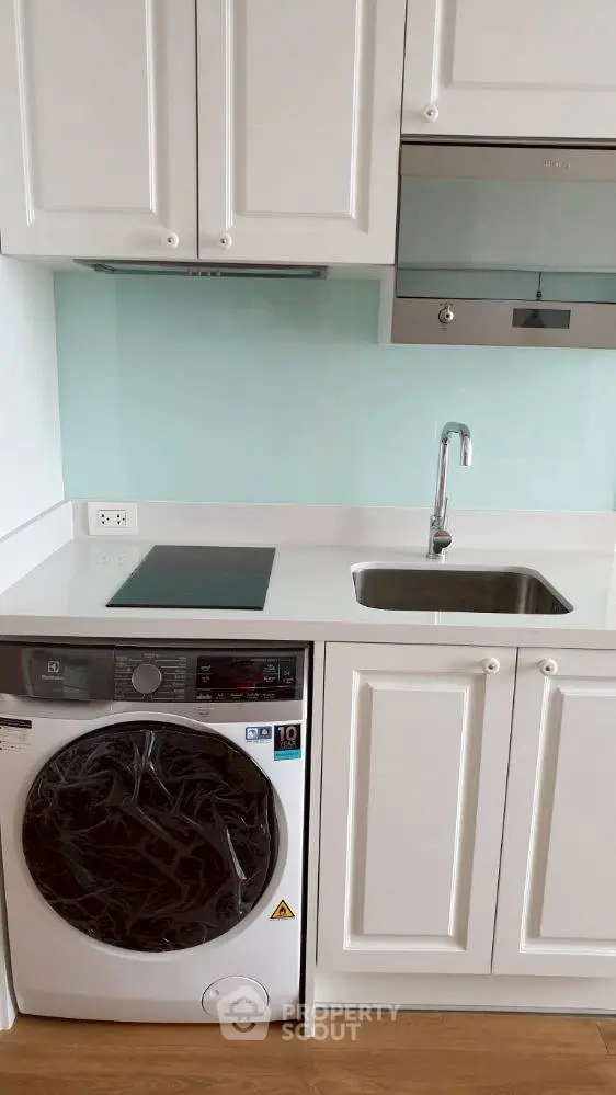 Modern kitchen with sleek white cabinets and built-in appliances, featuring a washing machine and electric stove.