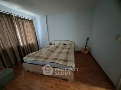 Cozy bedroom with wooden flooring and natural light, featuring a comfortable bed and a guitar for a relaxing ambiance.