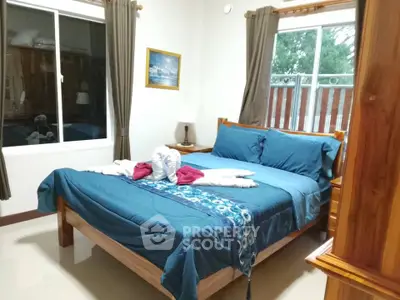 Cozy bedroom with wooden furniture and blue bedding, featuring large windows for natural light.