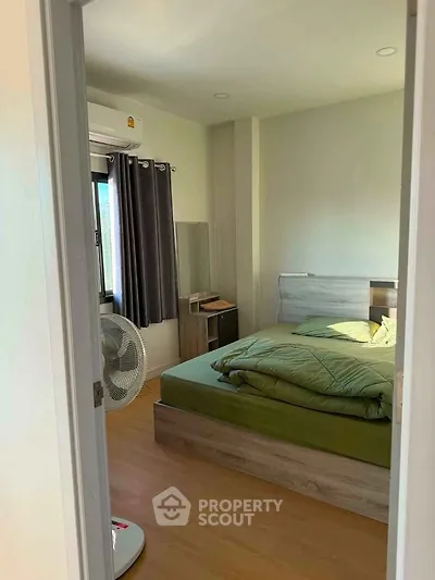 Cozy bedroom with wooden flooring and modern furnishings, featuring a large window for natural light.