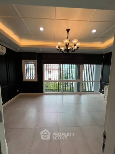 Spacious living room with elegant chandelier and large windows offering natural light.