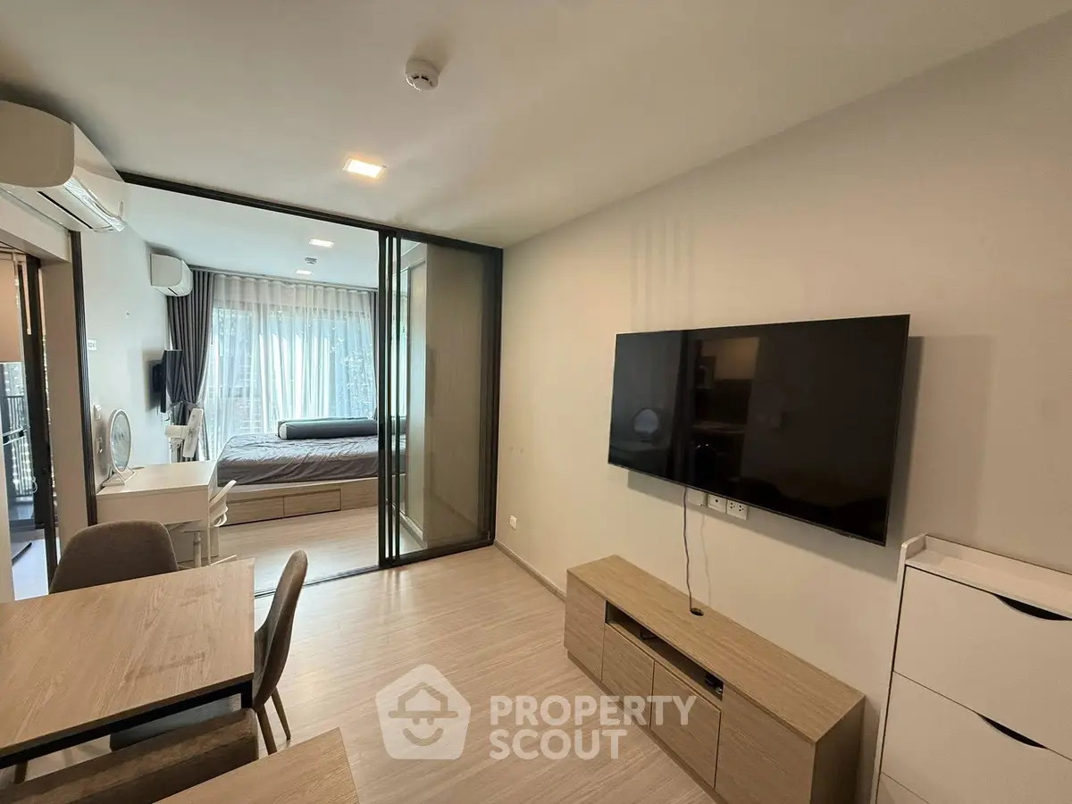 Modern living room with open layout and bedroom view, featuring sleek furniture and large TV.