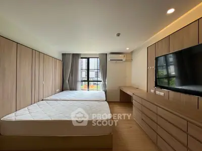 Spacious bedroom with twin beds, large TV, and ample storage in modern apartment.