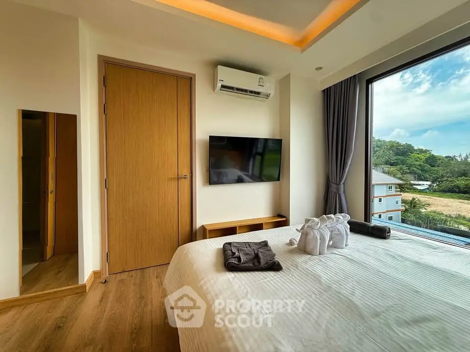 Modern bedroom with large window offering scenic view, featuring a wall-mounted TV and elegant decor.