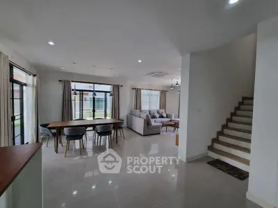 Spacious modern living room with dining area and staircase, featuring large windows and stylish decor.