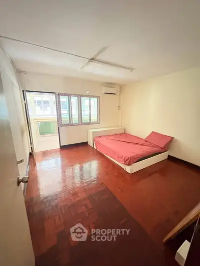 Spacious bedroom with wooden flooring and natural light, featuring a cozy bed and balcony access.