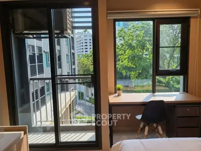 Modern bedroom with large windows offering a city view, featuring a sleek desk and comfortable chair.