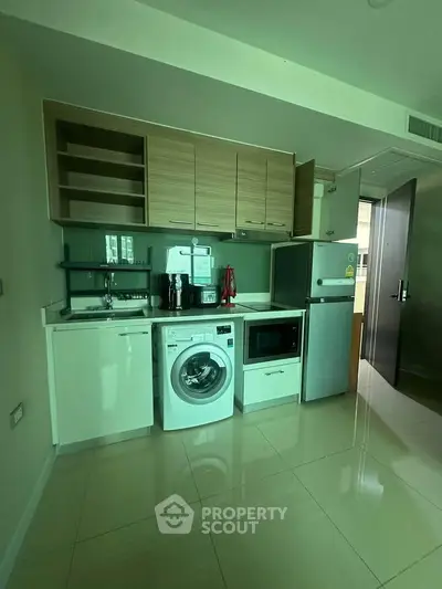 Modern compact kitchen with appliances including washing machine and microwave, sleek cabinetry, and tiled flooring.