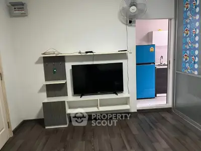 Modern living room with TV and open kitchen view, featuring stylish flooring and vibrant blue fridge.