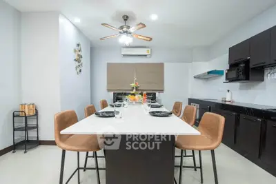 Modern kitchen with dining area, featuring sleek black cabinets and a stylish ceiling fan.