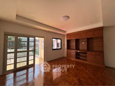Spacious living room with wooden flooring and built-in shelving, featuring large windows for natural light.