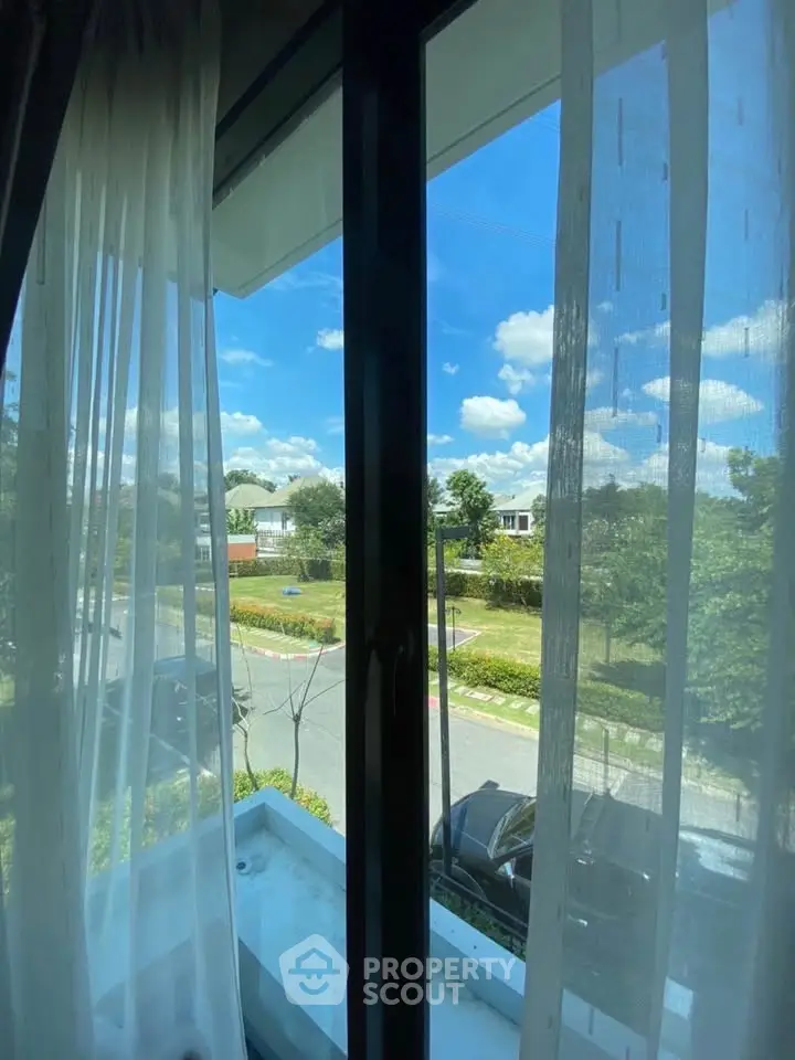 Bright window view showcasing a serene neighborhood with lush greenery and blue skies.