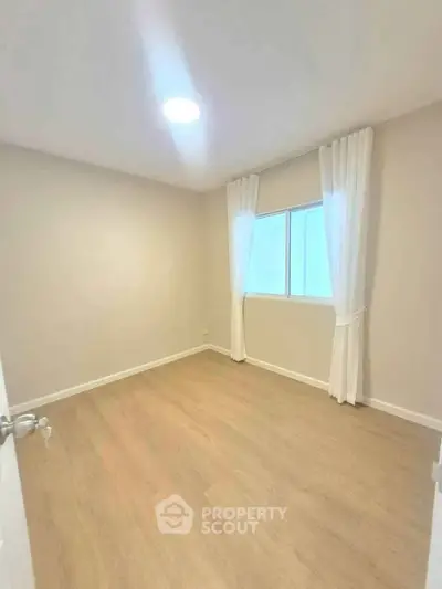 Spacious empty bedroom with wooden flooring and large window, perfect for customization.