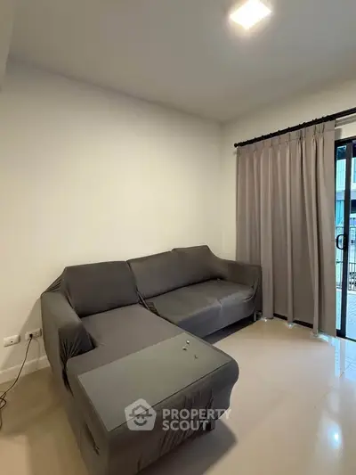 Cozy living room with modern gray sofa and sliding glass door leading to balcony.