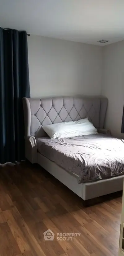 Elegant bedroom with a luxurious tufted bed, rich hardwood flooring, and sumptuous dark curtains creating a cozy and sophisticated ambiance.