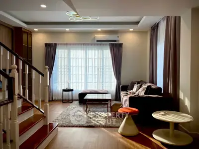 Elegant living room with modern decor and natural light, featuring a cozy seating area and stylish staircase.