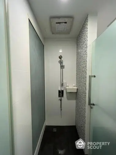 Sleek modern bathroom with a walk-in shower featuring mosaic tiles, a wall-mounted sink, and a frosted glass door for privacy.