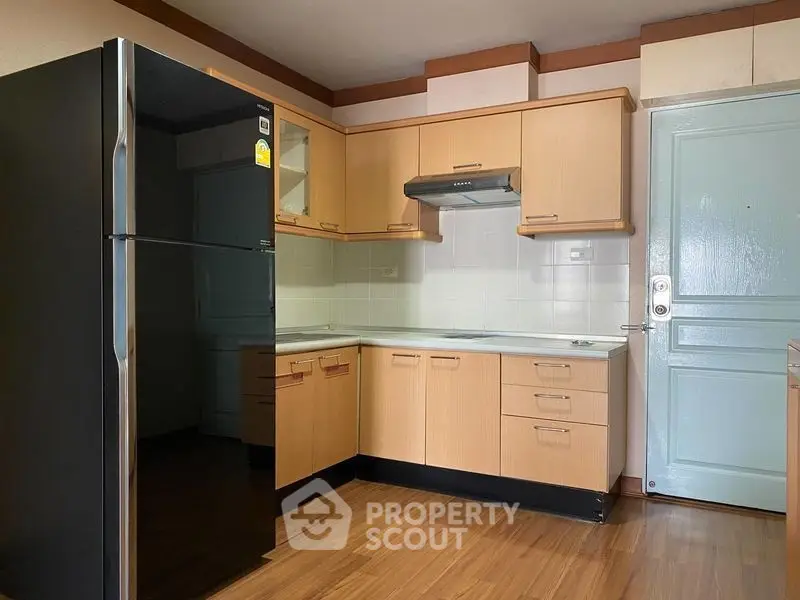 Modern kitchen with sleek black fridge and wooden cabinets in cozy apartment