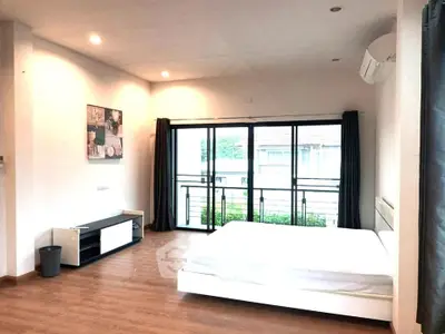 Spacious modern bedroom with large windows and balcony access, featuring sleek wooden flooring and minimalist decor.