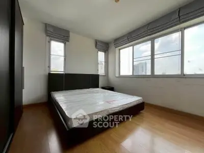 Spacious bedroom with large windows and wooden flooring in modern apartment.