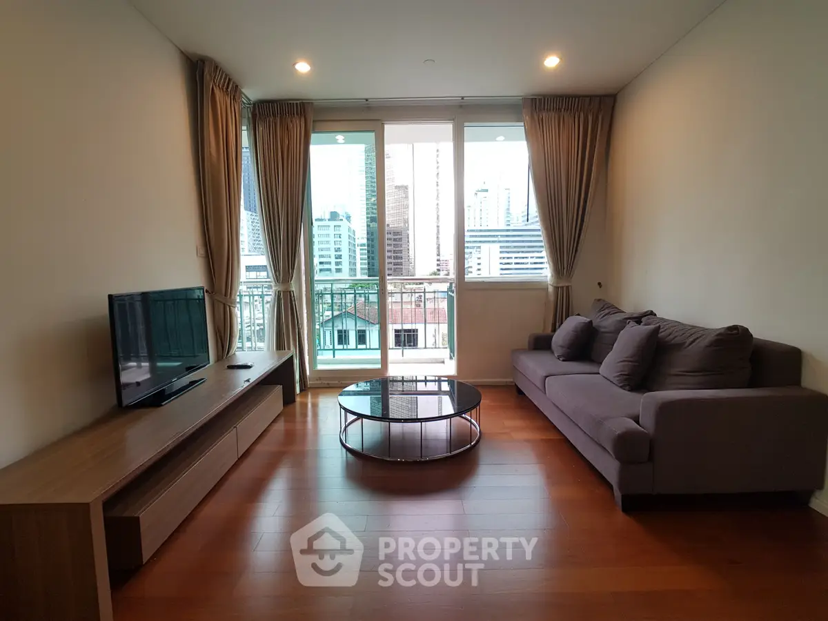 Spacious living room with modern furniture and city view balcony in high-rise apartment.