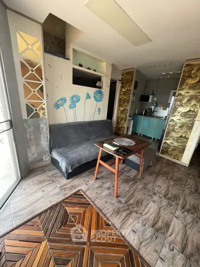 Charming living room with unique flooring and artistic wall design, featuring a cozy sofa and modern kitchenette.