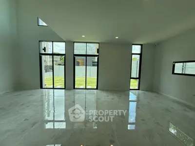 Spacious modern living room with high ceilings and large windows overlooking a lush garden.