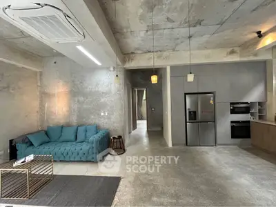Modern industrial-style living room with concrete walls and sleek kitchen appliances.