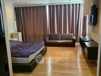 Spacious bedroom with wooden flooring, cozy sofa, and large windows with curtains.