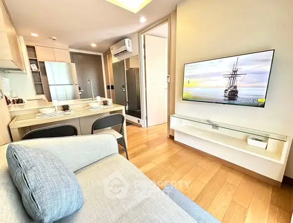 Modern living room with open kitchen, featuring sleek furniture and a wall-mounted TV.