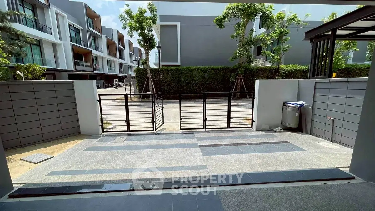 Modern townhouse entrance with sleek gate and driveway in sunny neighborhood