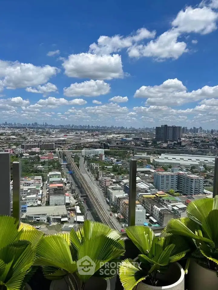 Stunning cityscape view from a high-rise balcony with lush greenery and clear blue skies.