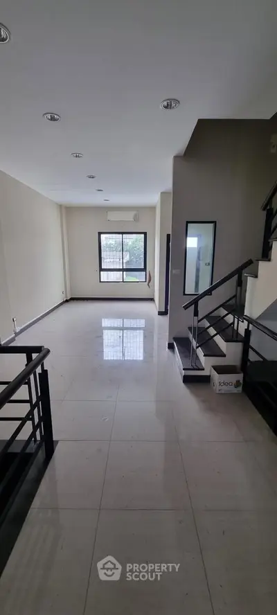 Spacious modern living room with sleek staircase and large window, perfect for stylish urban living.