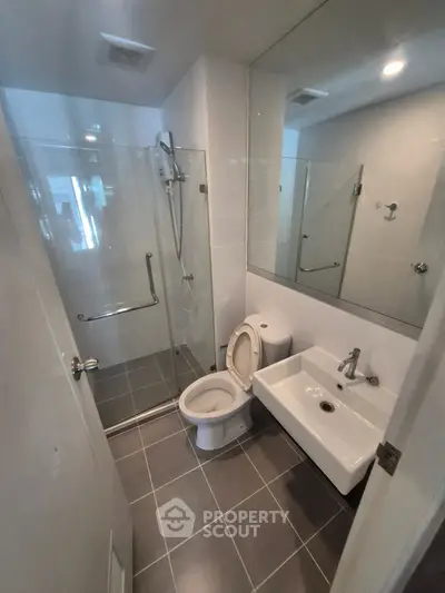 Modern bathroom with glass shower, sleek sink, and toilet in contemporary apartment.
