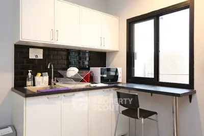 Modern compact kitchen with sleek black and white design, featuring a microwave and breakfast bar.