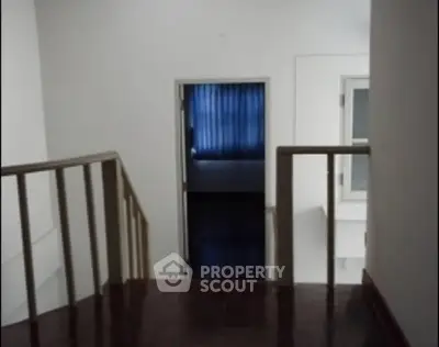 Spacious hallway leading to a room with blue curtains, featuring wooden flooring and railing.