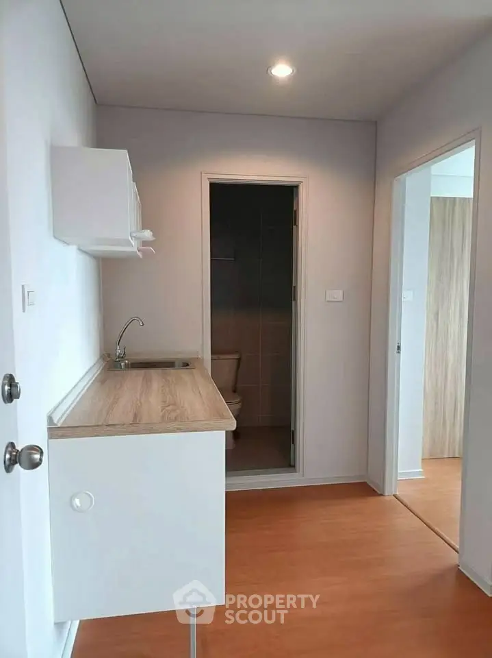 Compact kitchen area with wooden countertop and adjacent bathroom in modern apartment.