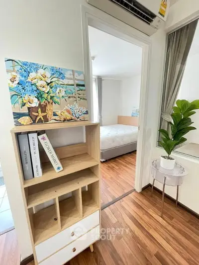 Cozy bedroom with wooden flooring and stylish decor, featuring a bookshelf and indoor plant for a welcoming ambiance.