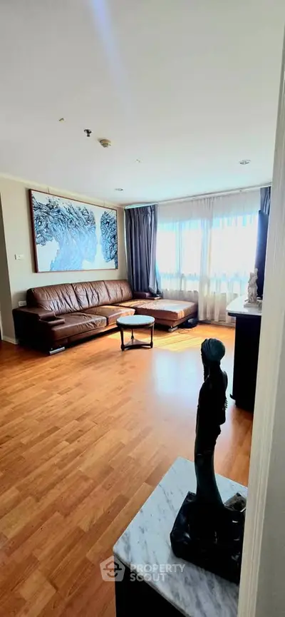 Spacious living room with elegant decor and natural light, featuring a leather sofa and artistic touches.