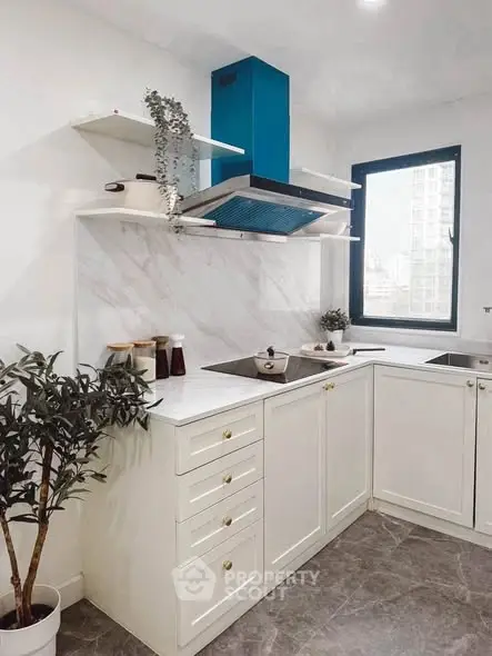 Modern kitchen with sleek white cabinets and marble backsplash, featuring a blue range hood and large window view.