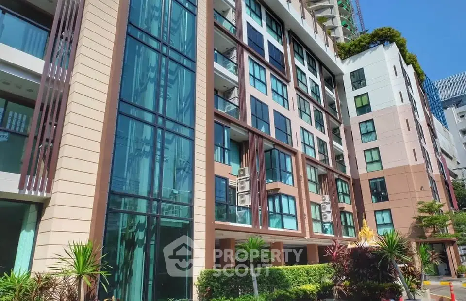 Modern apartment building with lush landscaping and large windows in urban setting.