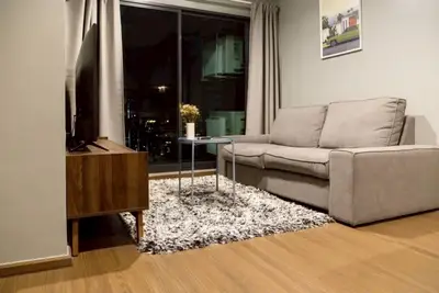 Modern living room with cozy sofa and stylish decor, featuring a large window with night city view.