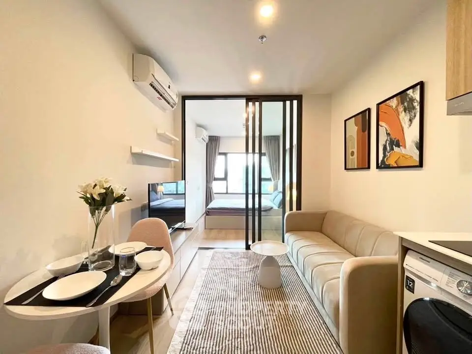 Modern living room with cozy sofa, dining area, and sliding glass doors leading to bedroom.