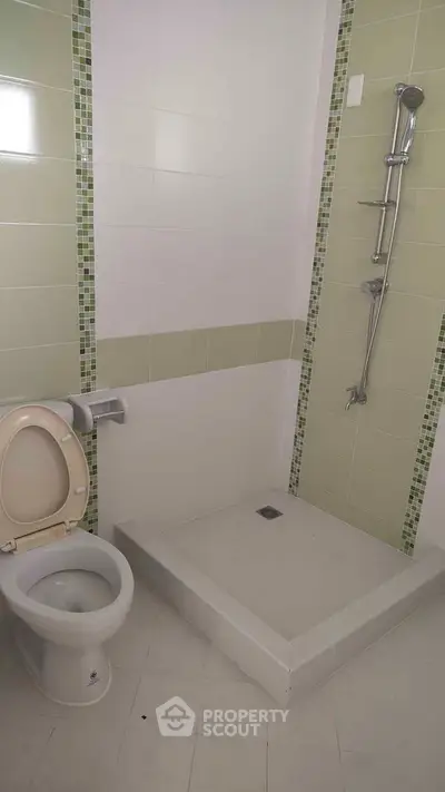 Modern bathroom with shower and toilet featuring green tile accents.