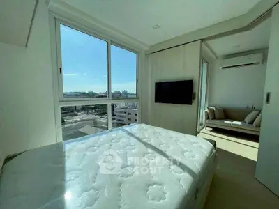 Bright bedroom with large window and city view, featuring a cozy adjacent living area.