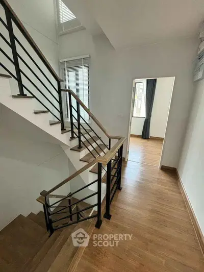 Modern staircase with wooden flooring and sleek railing in a bright interior space.