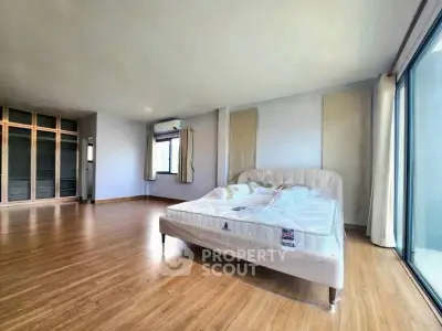 Spacious bedroom with large windows and wooden flooring in modern apartment.
